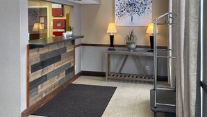 A hotel lobby with a reception desk, a ceiling fan, a painting, and a metal rack. - The Woodridge Inn (Connersville)