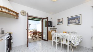 Una cocina con estufa, horno y comedor con mesa y sillas. Hay un reloj en la pared y una ventana con vistas.