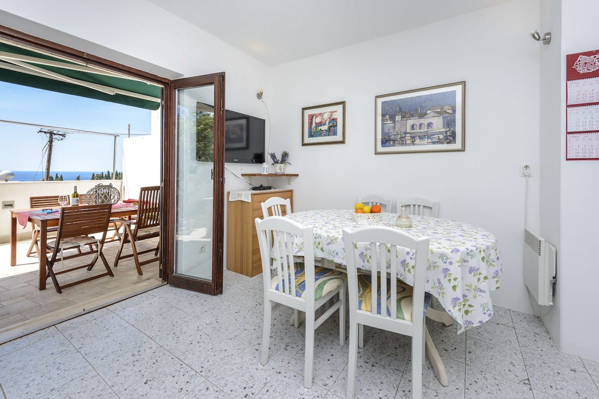 A dining area with a table and chairs, a television, and a view of the sea.