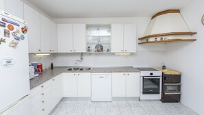 Una cocina con gabinetes blancos, lavavajillas, horno y pileta.