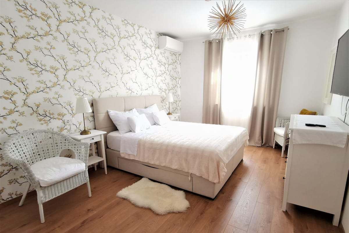 A bedroom with a bed, a chair, a desk, and a large window with curtains.