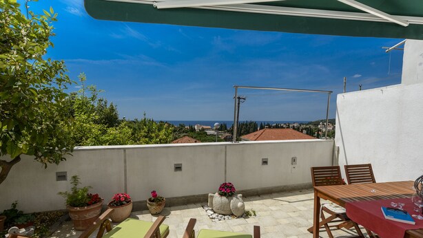 Una terraza con vistas al mar, una mesa con mantel rojo y sillas de madera.