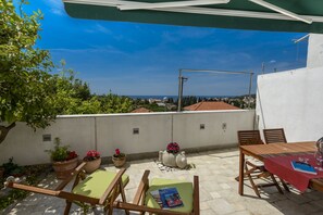 Una terraza con vistas al mar, una mesa con mantel rojo y sillas de madera.