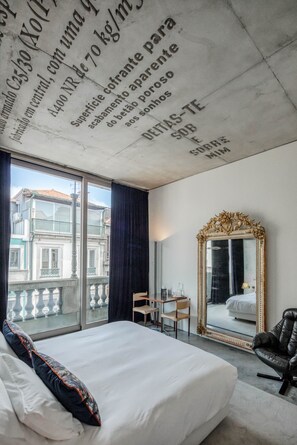 A hotel room with a large bed, a desk, a chair, a mirror, and a view of buildings through the window. - Hotel Casa do Conto - Arts & Residence (Porto)