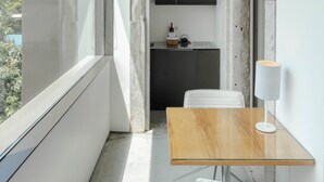 Un balcon avec une table en bois et une chaise blanche, un coin cuisine avec des placards, et une vue sur la verdure.