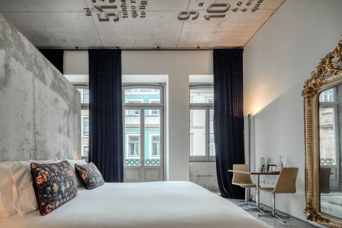 A modern hotel room with a large bed, two decorative pillows, a desk with a chair, and a large mirror.