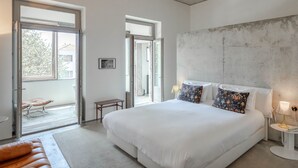 Une chambre moderne avec un grand lit, deux lampes de chevet et une vue sur l’extérieur grâce à une grande fenêtre.