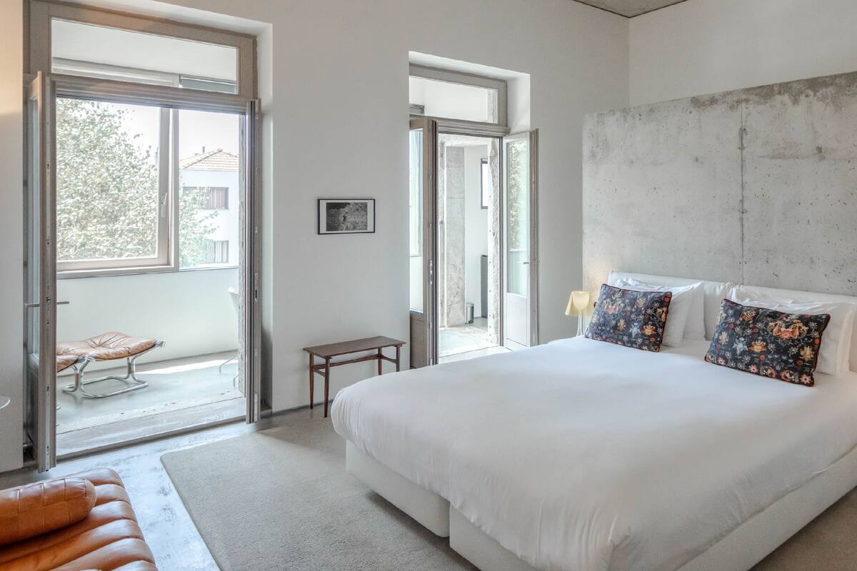 A modern bedroom with a large bed, two bedside lamps, and a view of the outside through a large window.