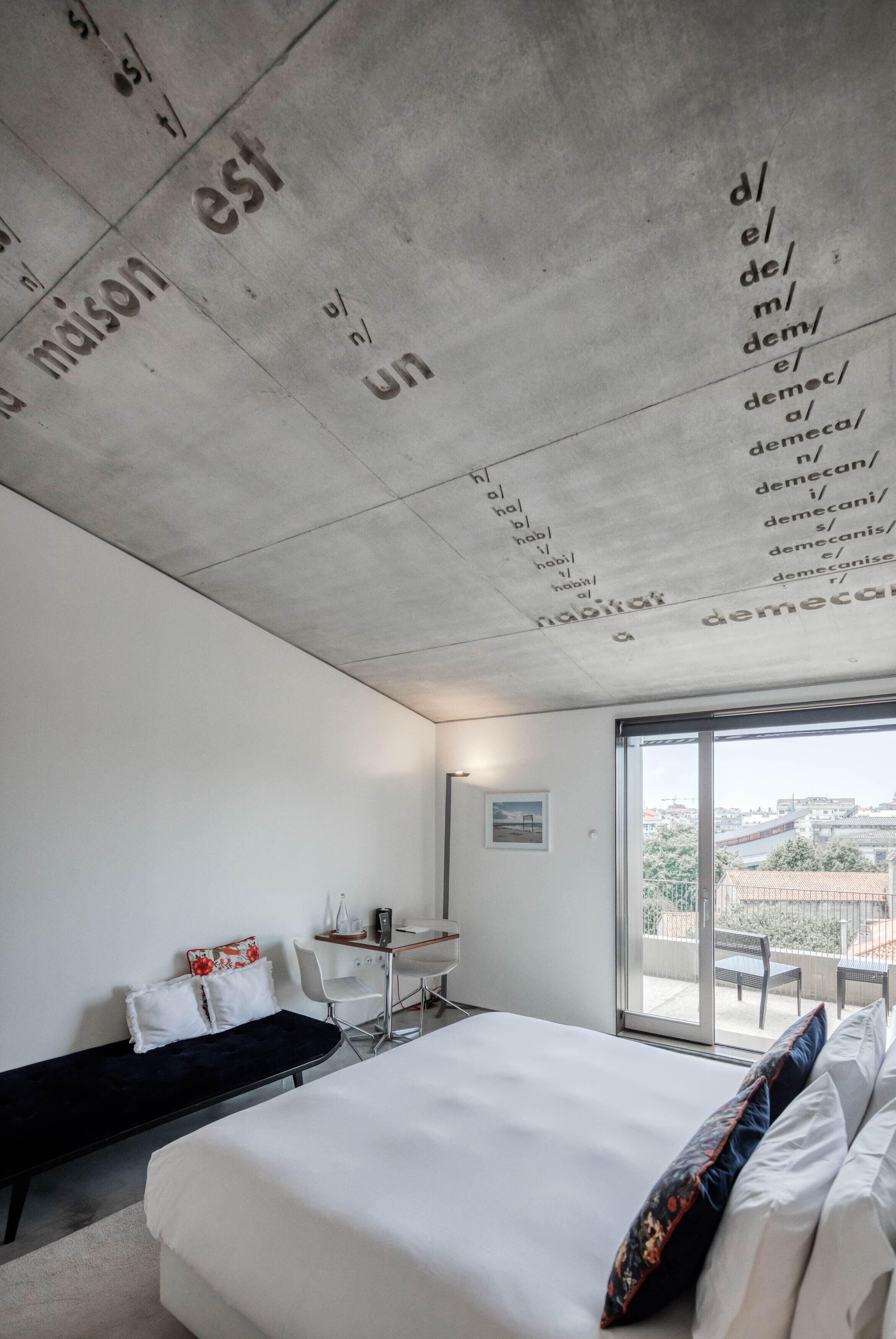 A modern hotel room with a large bed, a desk, and a balcony with a view of the city.
