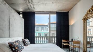 A bedroom with a large bed, two decorative pillows, a view of buildings through a balcony, and a large mirror.