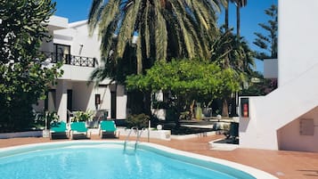 Una piscina al aire libre, sombrillas, sillones reclinables de piscina