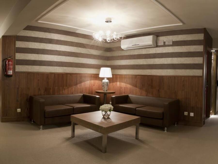 Un hall d’hôtel avec un mur décoré de motifs rayés, un espace salon central comprenant deux canapés et une table basse, ainsi qu’un lustre.