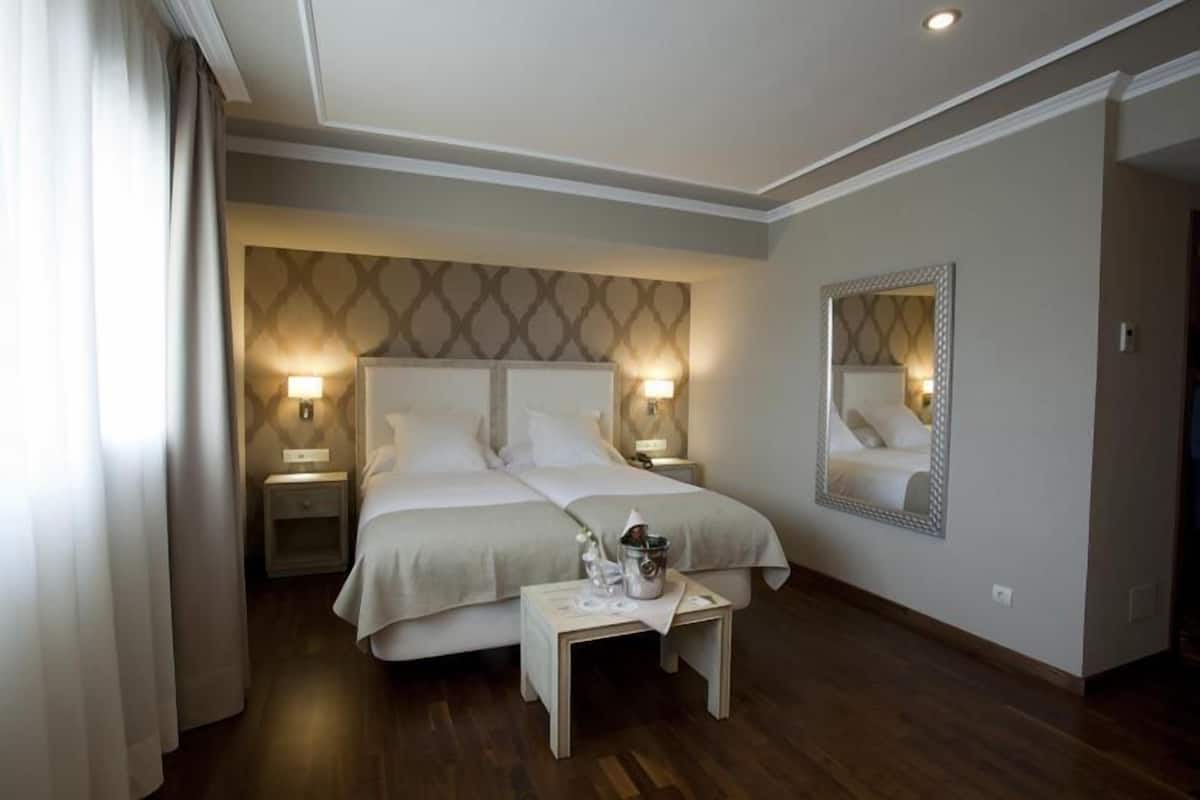 Habitación de hotel con cama doble, dos mesitas de noche, un tocador, un espejo y una pequeña mesa con lámpara.