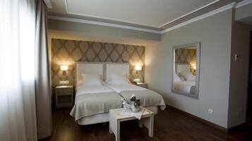 Habitación de hotel con cama doble, dos mesitas de noche, un tocador, un espejo y una pequeña mesa con lámpara.