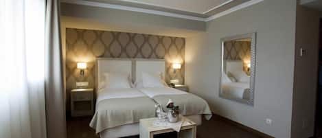 A hotel room with a double bed, two bedside tables, a nightstand, a mirror, and a small table with a lamp.