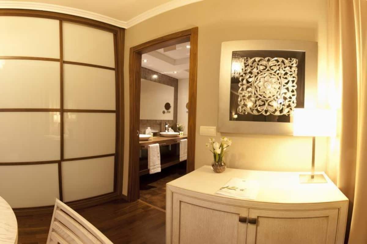 Habitación de hotel con una mesa de comedor redonda, un baño independiente con tocador y una cama con cabecero.