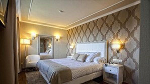 Una habitación de hotel con una cama grande, lámparas de noche, una mesita de noche y un espejo.