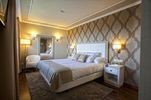 Una habitación de hotel con una cama grande, lámparas de noche, una mesita de noche y un espejo.