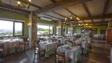 A restaurant with multiple tables set for dining, large windows offering a view of the outdoors, and a rustic interior with exposed wooden beams.