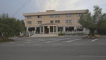 Un hotel de varios pisos con entrada central, aparcamiento y zona ajardinada con árboles.