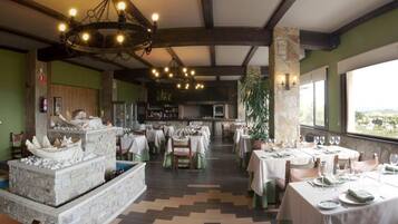 Un restaurant doté de nombreuses tables dressées pour le service, d’une cheminée en pierre et offrant une vue sur le paysage.