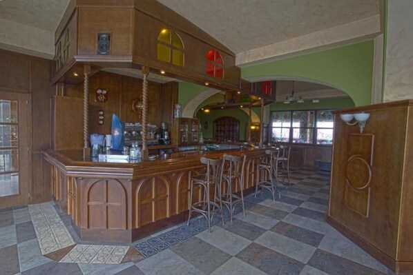 Una zona de bar con mostrador de madera, taburetes y suelo a cuadros.