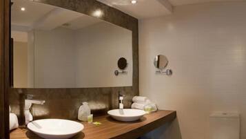 Un baño moderno con tocador de madera, dos lavamanos, un espejo grande y un inodoro.