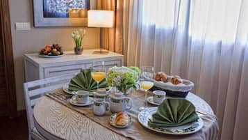 A breakfast table set with a variety of food items, including fruits, pastries, and beverages, in a well-lit room with a view of the outdoors.