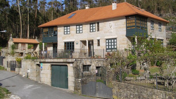 A stone building with a red-tiled roof, multiple windows, and a gated entrance. - Casa Rural A Rega (Poio)