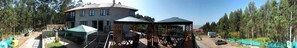 A stone house with a curved roof, outdoor seating area with tables and chairs, and a covered patio. - Casa Rural A Rega (Poio)