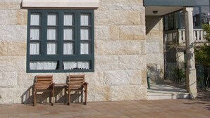 A stone building with a tiled roof, a window with curtains, and two wooden chairs outside. - Casa Rural A Rega (Poio)