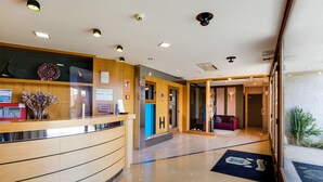 A hotel reception area with a wooden reception desk, a glass partition, and a blue sign with an 'H'. - Hotel Rural Campaniola (Pontevedra)