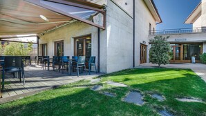 An outdoor patio with tables and chairs, a covered seating area, and a well-maintained lawn with stepping stones. - Hotel Rural Campaniola (Pontevedra)