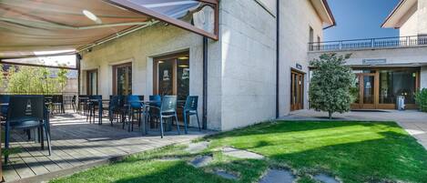 Un patio al aire libre con mesas y sillas, una zona de estar cubierta y un césped cuidado con piedras para caminar.