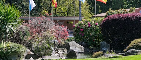Un jardín con diversas plantas, una formación rocosa y tres banderas.