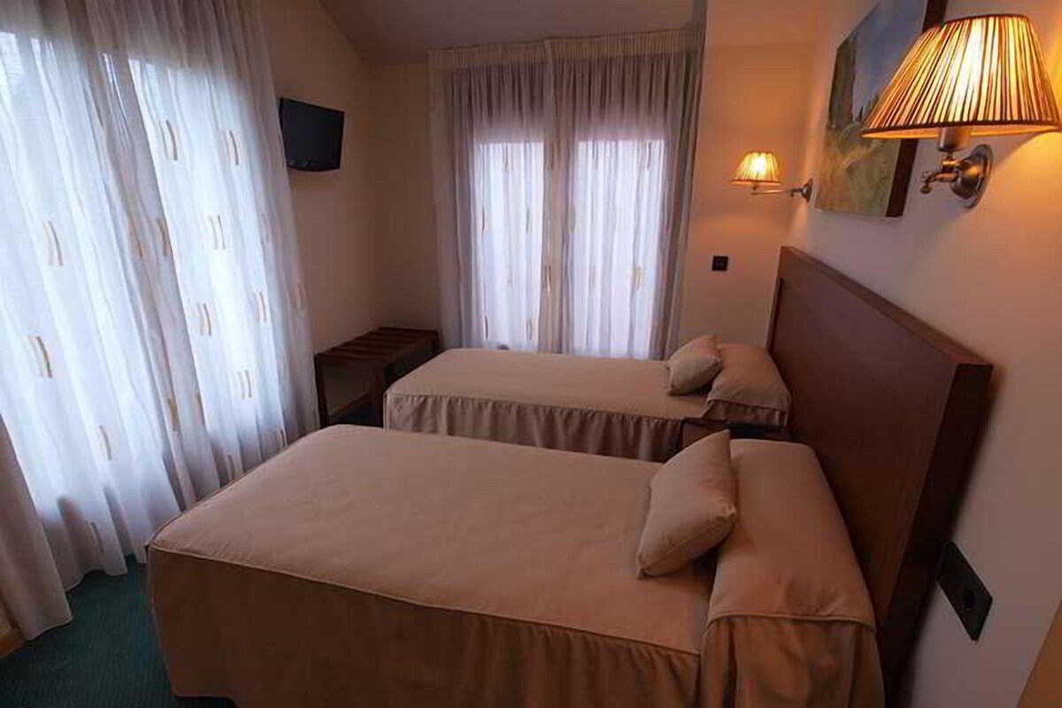 Una habitación de hotel con dos camas, televisión, lámpara y un cuadro en la pared.