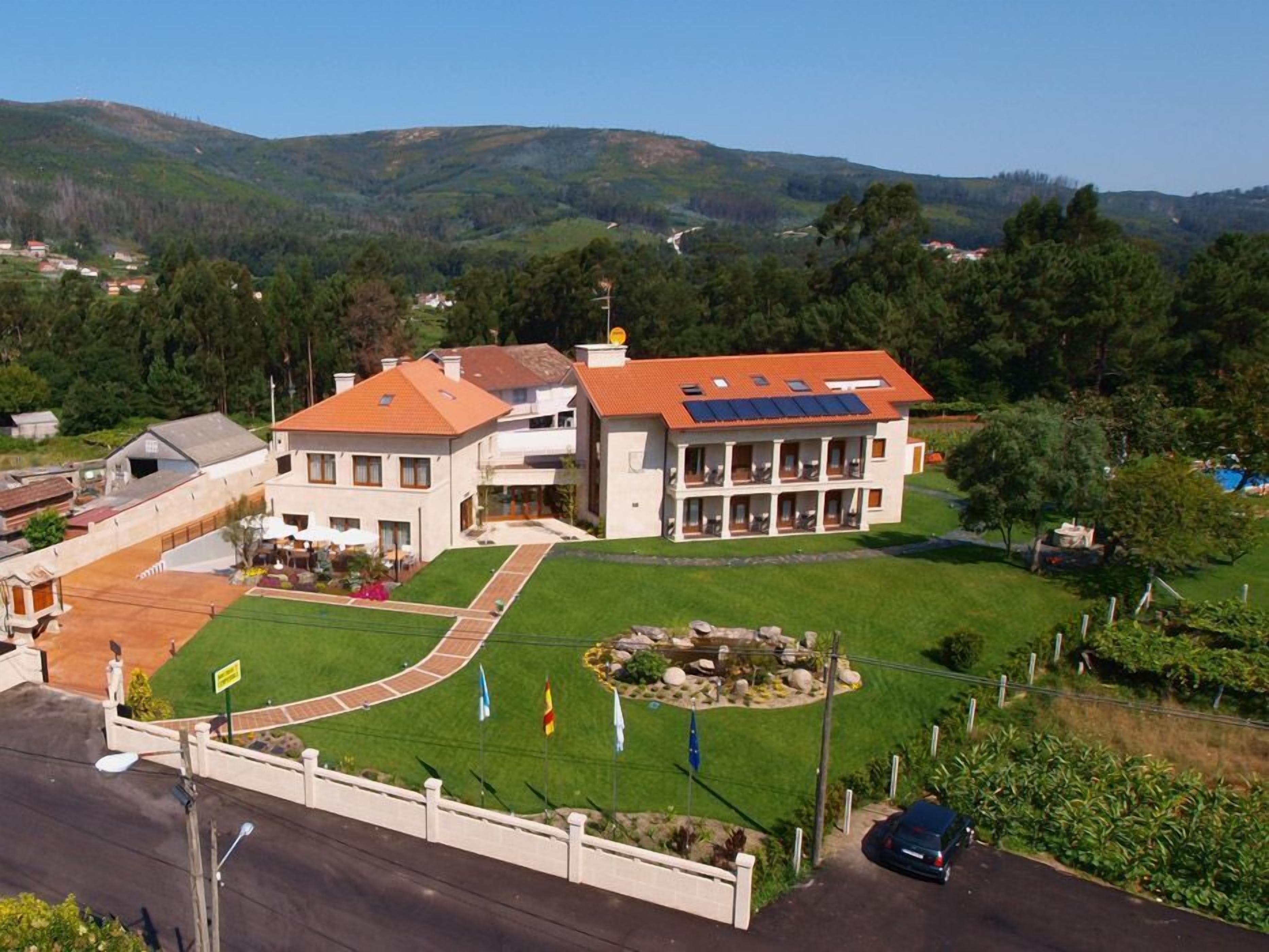 Um edifício grande e moderno com telhado de telhas vermelhas, várias varandas e um gramado bem cuidado.
