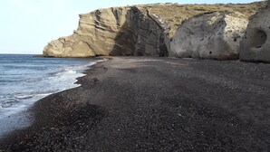 A coastal landscape with a rocky cliff and a pebbly beach. - Sun Anemos Resort (Santorini)