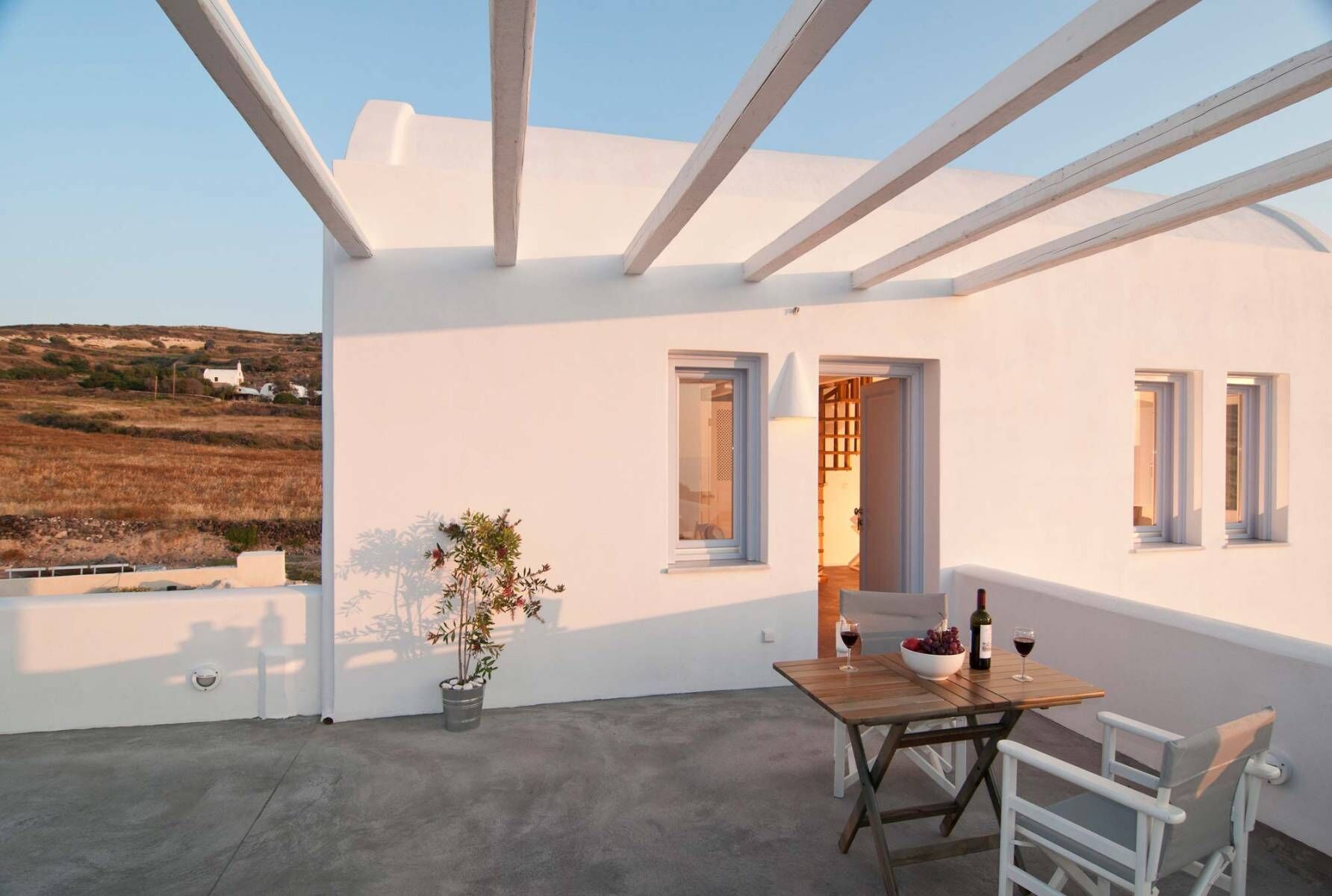 A rooftop terrace with a table set for two, a potted plant, and a view of a rural landscape.