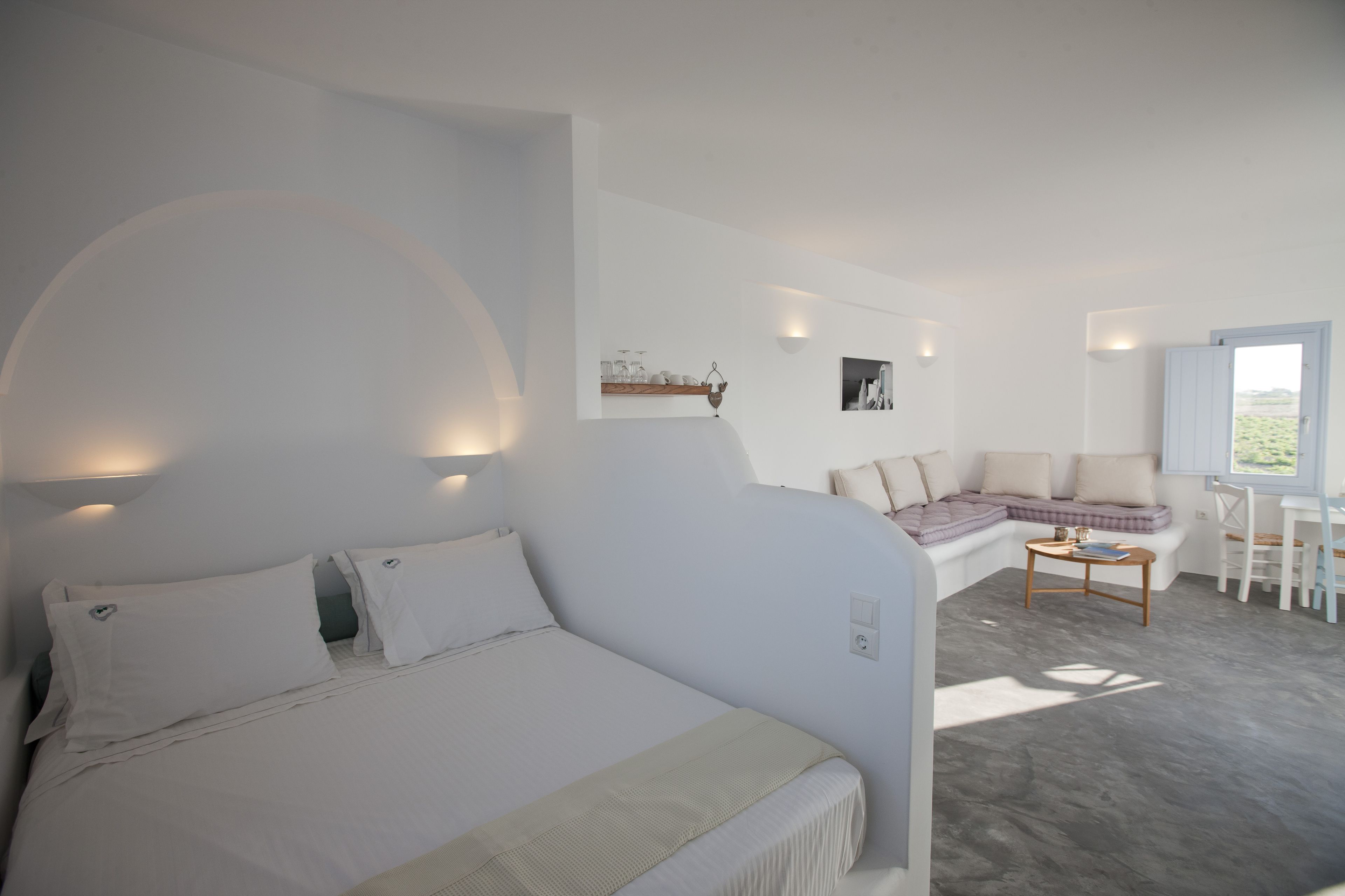 Een moderne slaapkamer met een groot bed, een zithoek met een bank en fauteuils, een kleine tafel, en een raam met uitzicht.