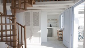 A staircase leading to a second floor, a kitchen with white cabinets and a stainless steel dishwasher, and a sliding glass door leading to an outdoor area. - Sun Anemos Resort (Santorini)