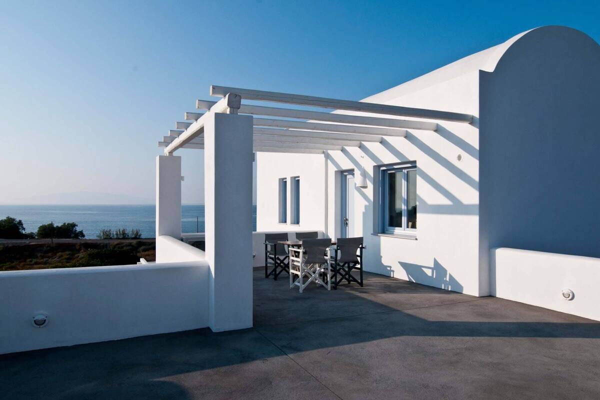 A white building with a covered patio, a table, and chairs.