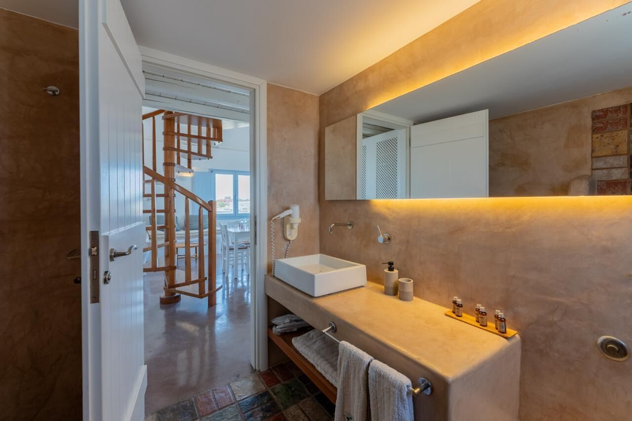 Casa de banho moderna com lavatório branco, um espelho grande e escada de madeira para outro quarto.