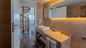 A modern bathroom with a white sink, a large mirror, and a wooden staircase leading to another room. - Sun Anemos Resort (Santorini)