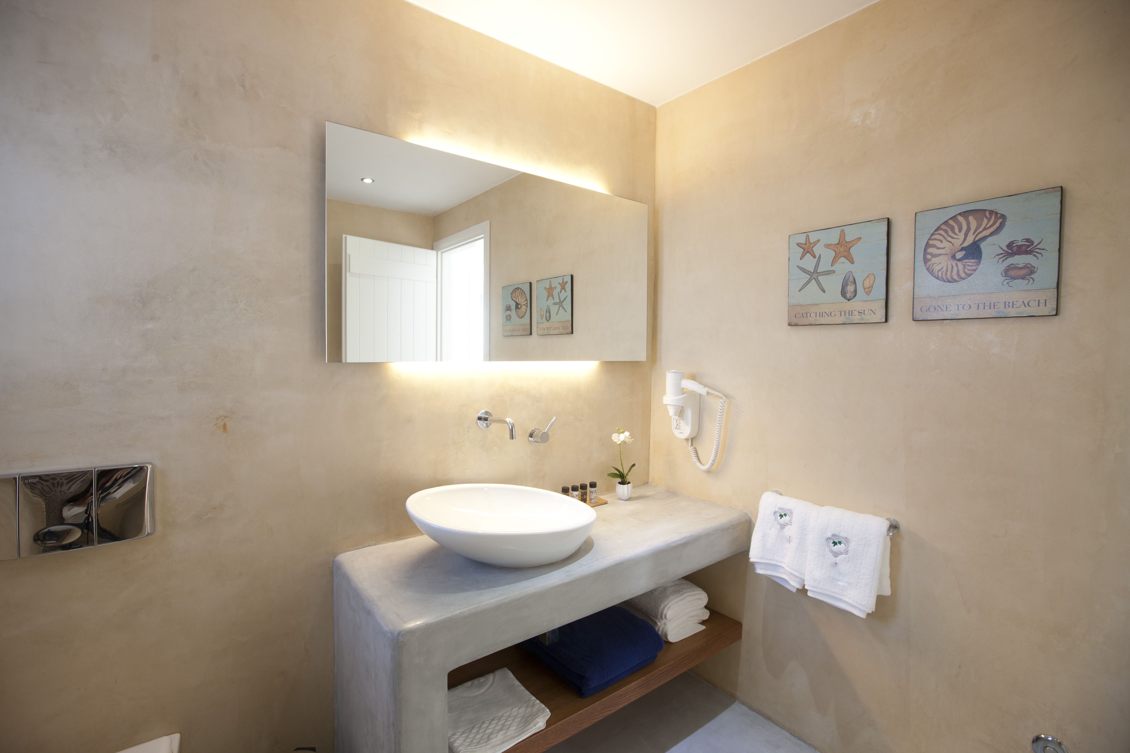 A modern bathroom with a large mirror, a white sink, and two wall-mounted artworks depicting sea creatures.