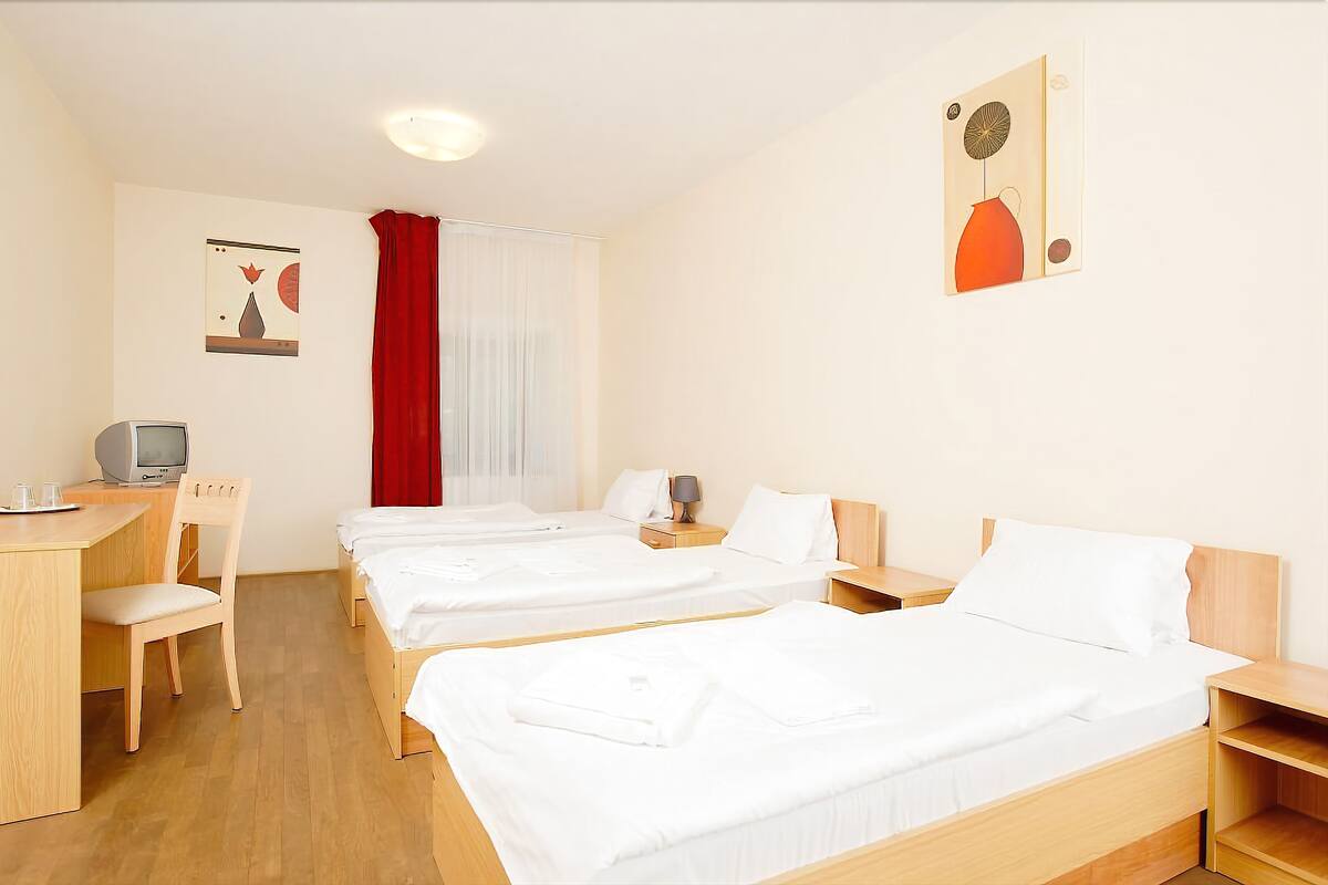 Une chambre d’hôtel avec deux lits simples, un bureau avec une chaise, une télévision et un rideau rouge.