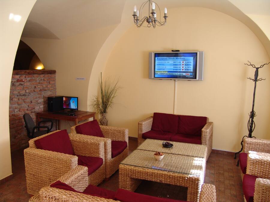 Un salón acogedor con muebles de mimbre, un televisor mostrando información del mercado de valores, y una pared de ladrillo.