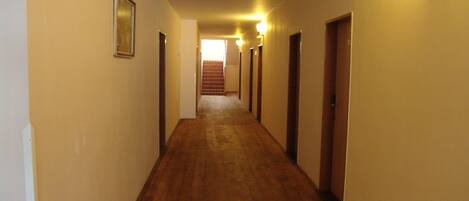 A hallway with wooden floors and doors on both sides, leading to a staircase at the end.