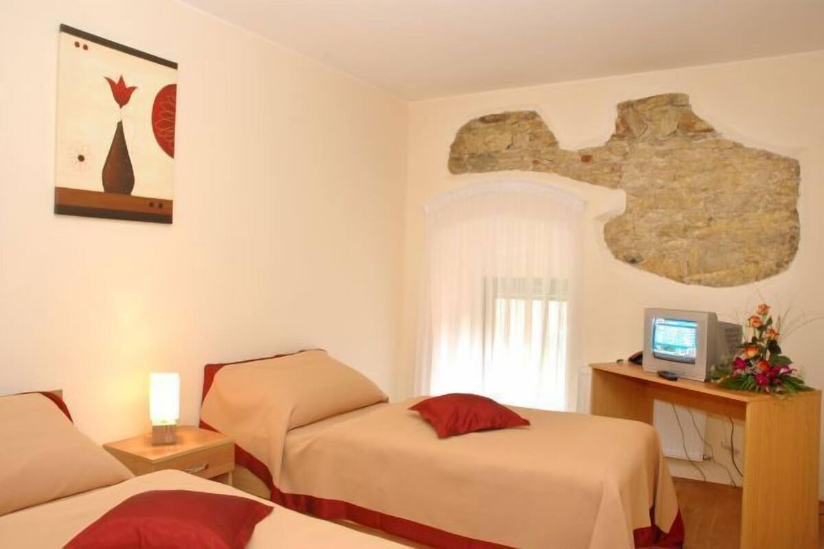 Une chambre d’hôtel avec deux lits, un mur en pierre, un téléviseur et un tableau accroché au mur.