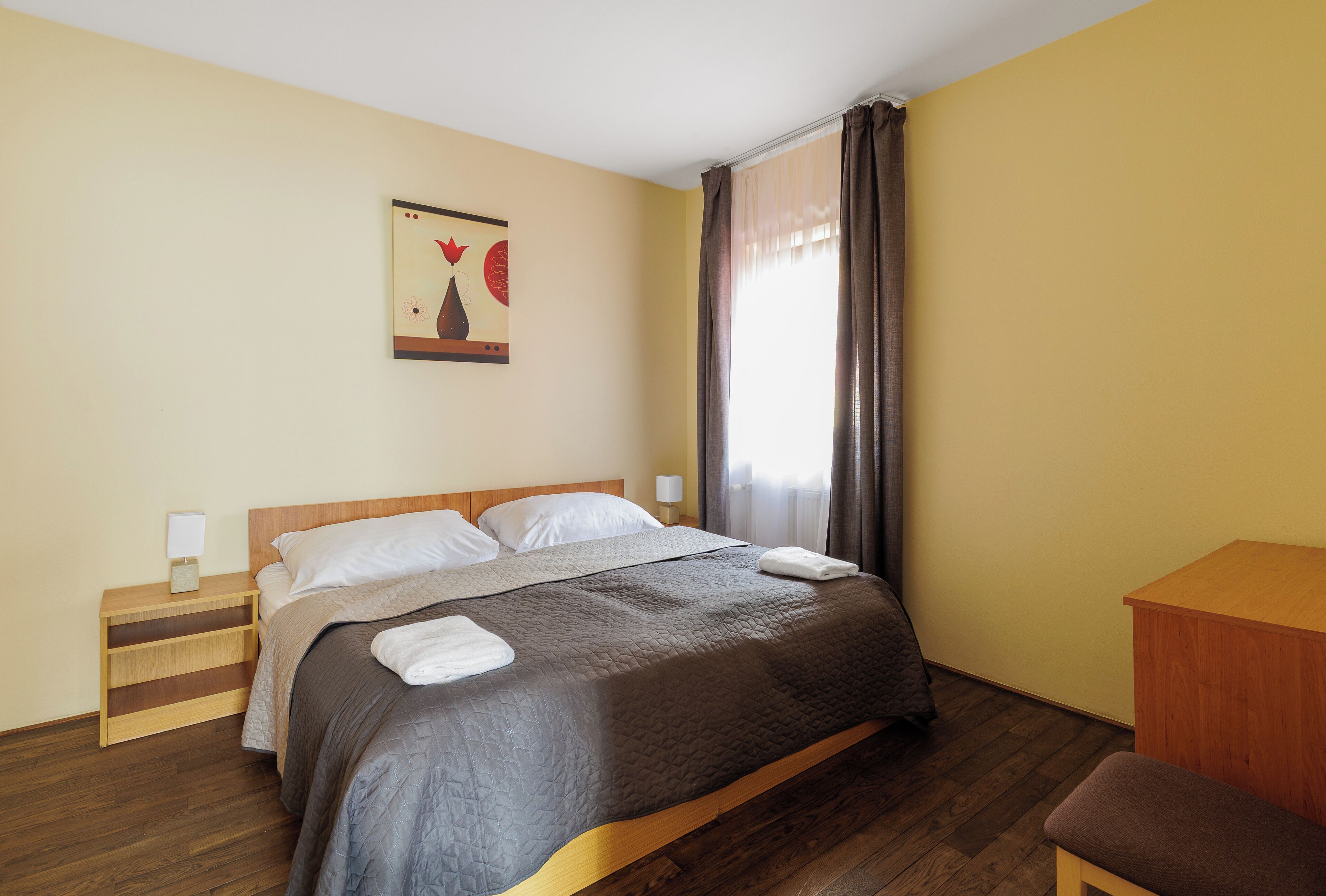 A neatly made bed with a wooden headboard, a bedside table with a lamp, and a wall-mounted artwork.
